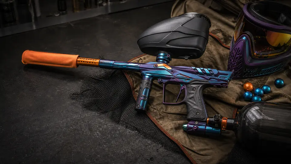 A colorful paintball marker with a loader, air tank and orange barrel cover resting on a collector workbench.