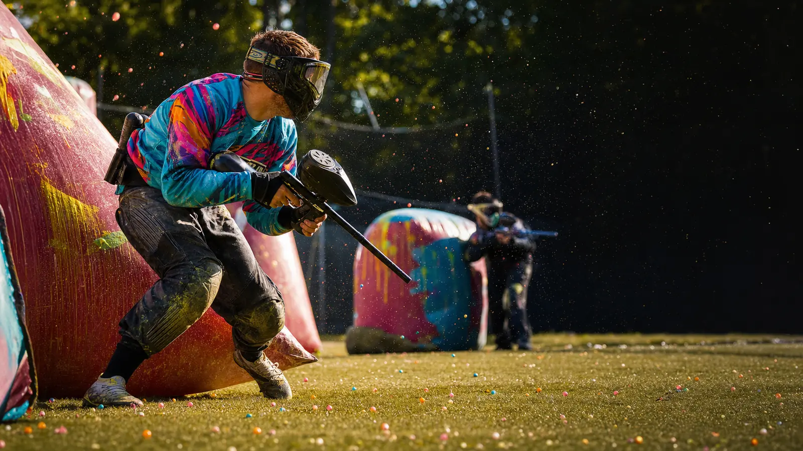 A masked paintball athlete moves past a colourful field bunker while keeping their marker pointed safely downfield.